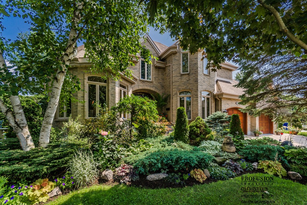 Large traditional beige two-story brick exterior home idea in Montreal with a gambrel roof
