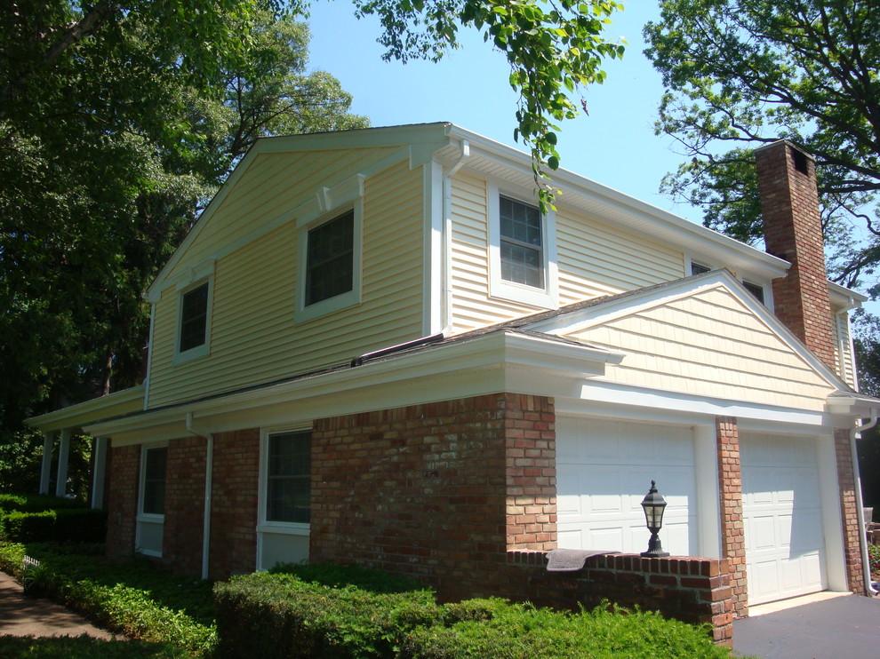 Foto della facciata di una casa grande gialla classica a due piani con rivestimento in vinile e tetto a capanna