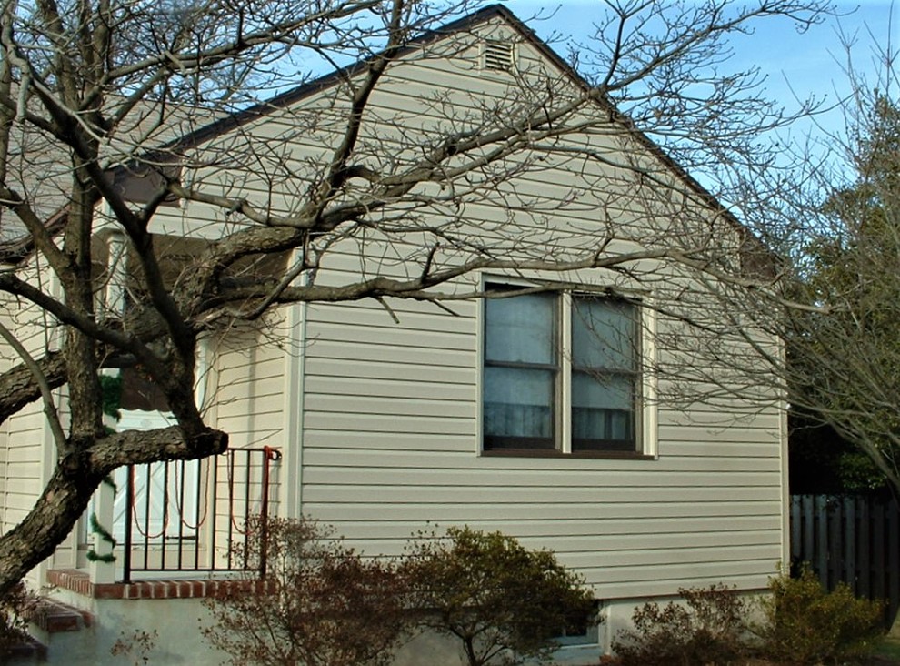 Foto på ett litet 60 tals beige hus, med två våningar och vinylfasad