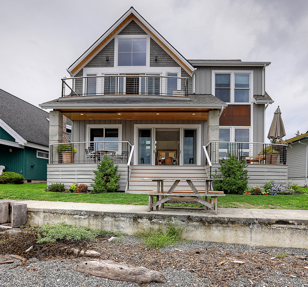 Gey beach style two floor detached house in Seattle with a pitched roof, wood cladding, a shingle roof, a grey roof and board and batten cladding.