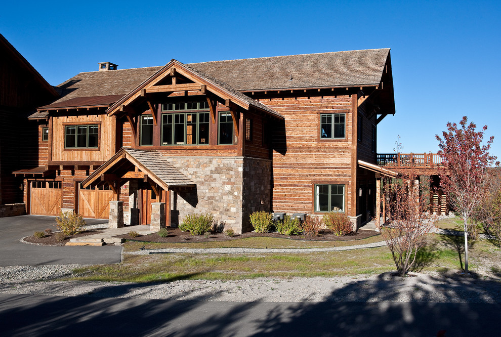 Esempio della villa grande marrone rustica a due piani con rivestimento in legno, tetto a capanna e copertura a scandole
