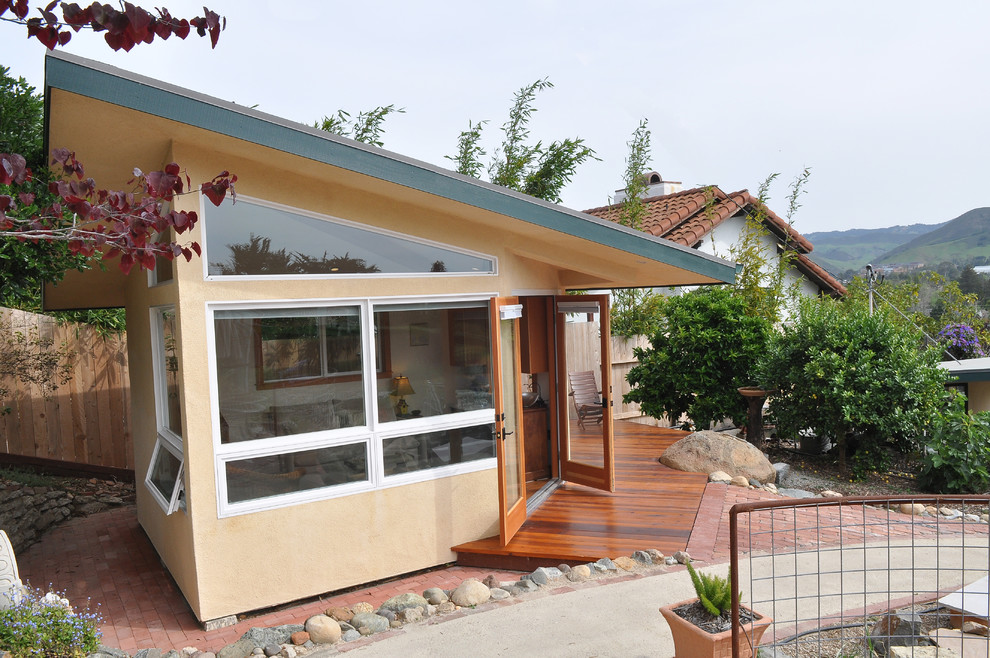 Aménagement d'une petite façade de maison beige contemporaine en stuc de plain-pied avec un toit plat et un toit en métal.