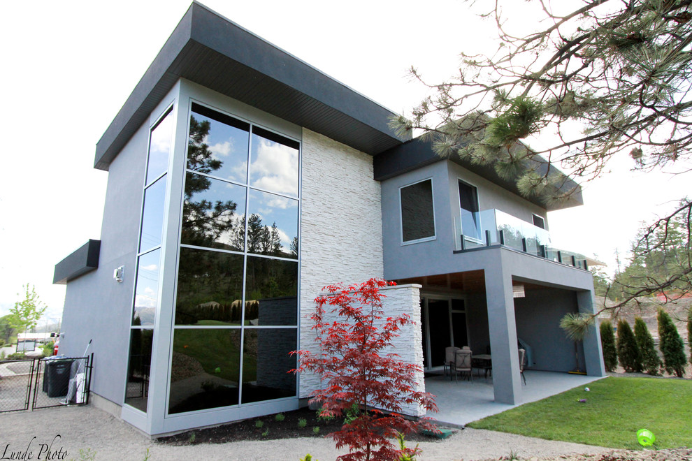 Idée de décoration pour une façade de maison grise minimaliste en stuc de taille moyenne et à un étage.