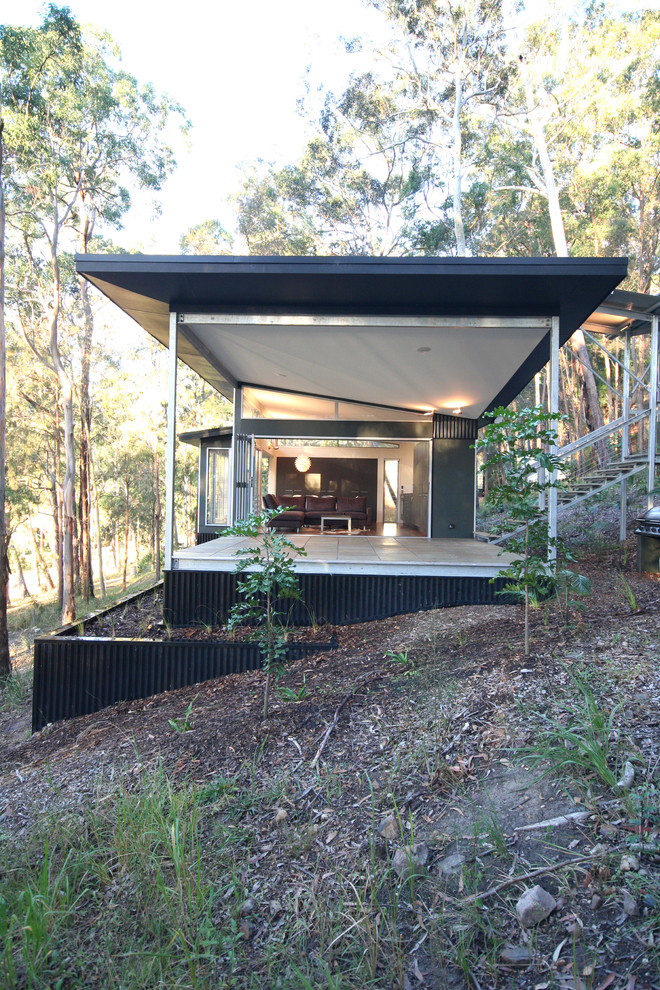 Réalisation d'une petite façade de maison métallique et noire minimaliste de plain-pied avec un toit plat.