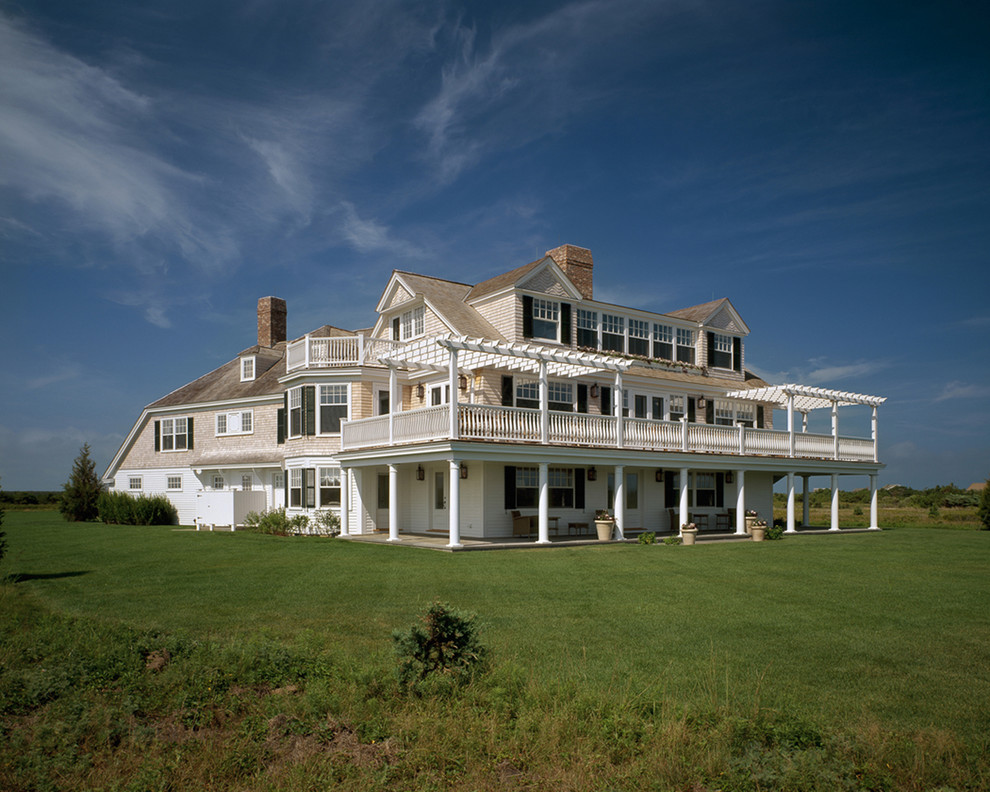 Esempio della villa ampia beige stile marinaro a tre piani con rivestimento in legno e copertura a scandole