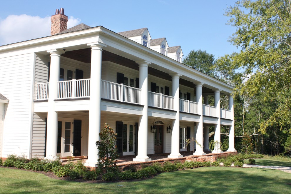 Esempio della facciata di una casa grande bianca classica a due piani con tetto a padiglione e rivestimento in vinile