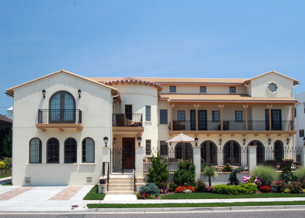На фото: большой, трехэтажный, бежевый дом в средиземноморском стиле с облицовкой из цементной штукатурки и двускатной крышей с