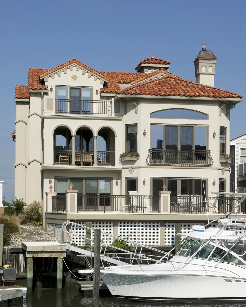 Diseño de fachada beige mediterránea grande de tres plantas con revestimiento de estuco y tejado a dos aguas