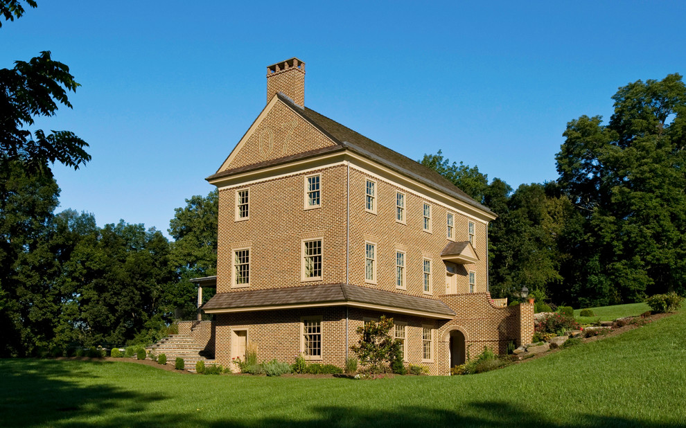 Immagine della facciata di una casa country a tre piani con rivestimento in mattoni e tetto a capanna