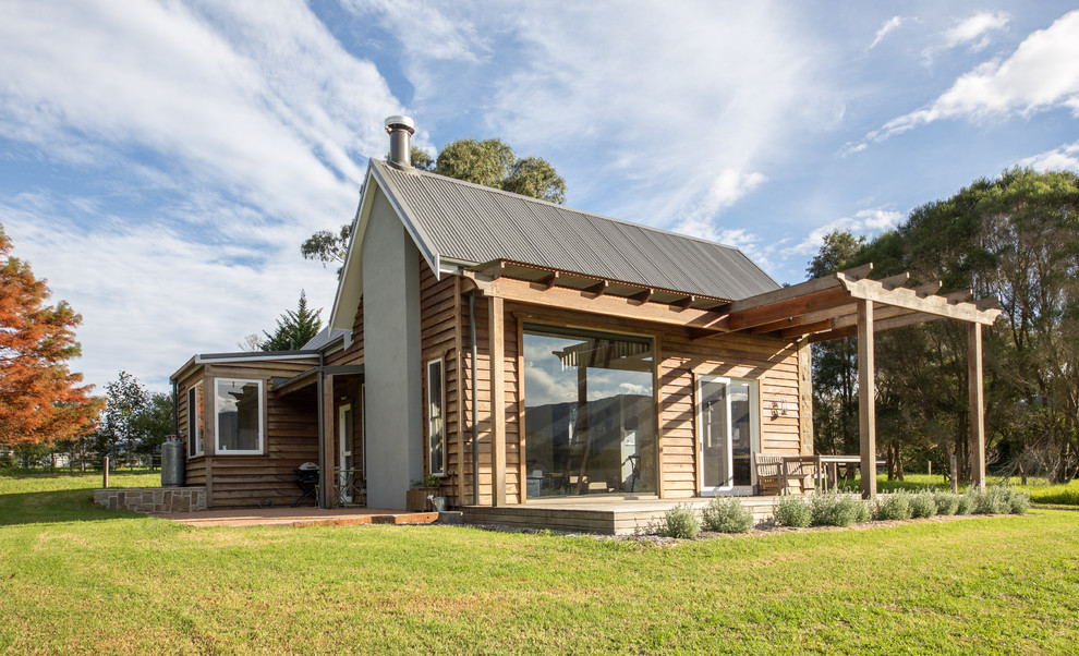 Cette photo montre une petite façade de maison nature en bois à un étage avec un toit à deux pans et un toit en métal.