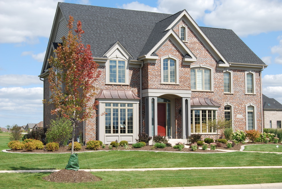 Cette photo montre une grande façade de maison rouge chic en brique à un étage avec un toit à deux pans et un toit en shingle.