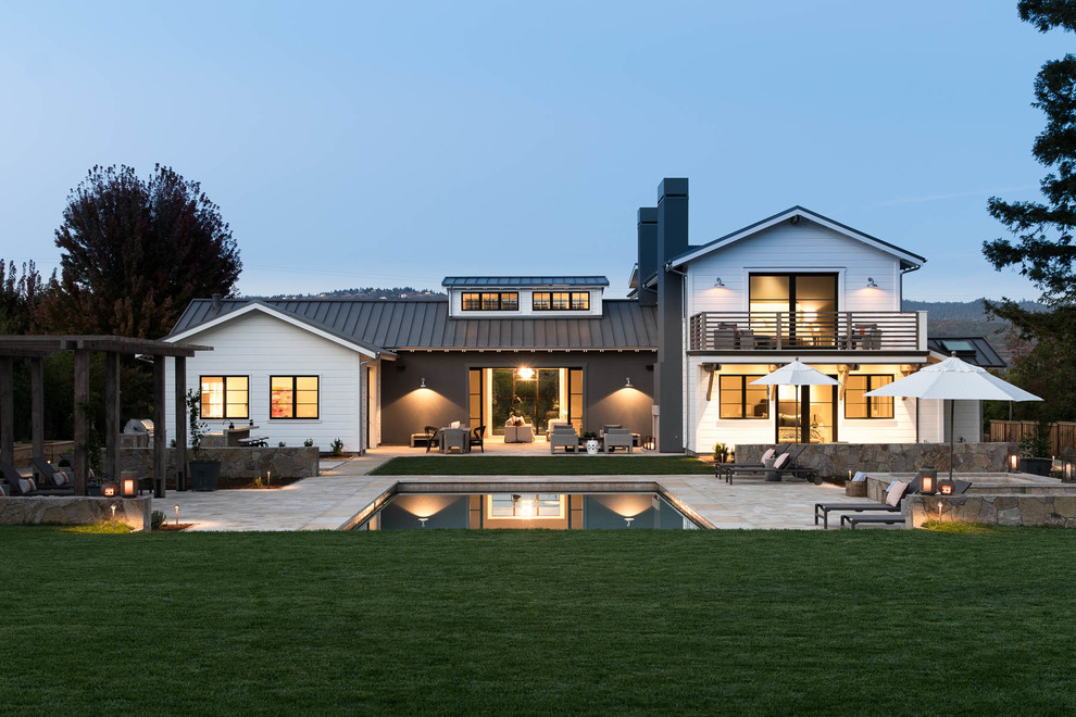 Idée de décoration pour une grande façade de maison blanche champêtre à un étage avec un revêtement en vinyle, un toit à deux pans et un toit en métal.