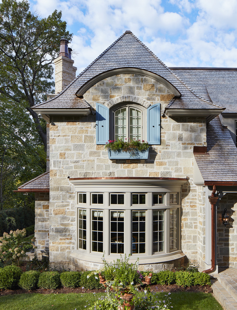 Aménagement d'une grande façade de maison multicolore classique en pierre à un étage avec un toit à quatre pans et un toit en shingle.