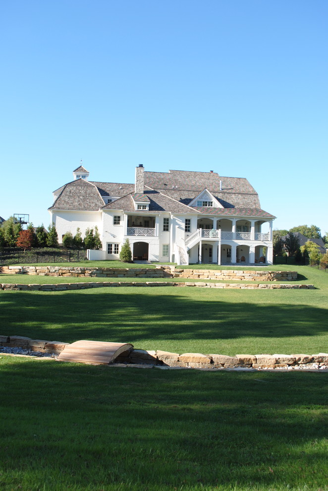 Immagine della facciata di una casa bianca country a due piani con terreno in pendenza