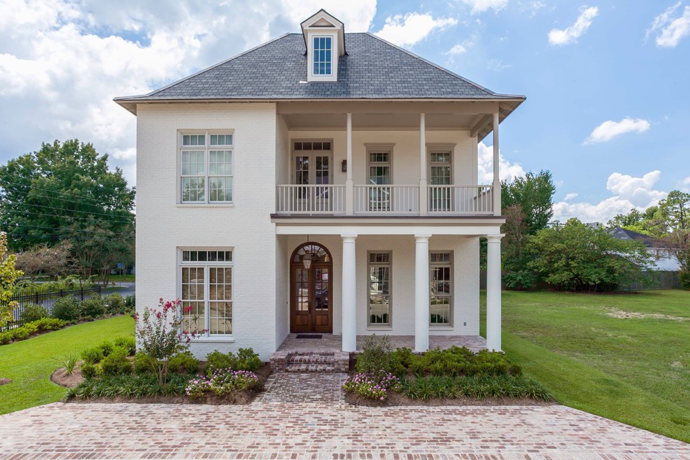 Inspiration for a mid-sized timeless white two-story brick house exterior remodel in New Orleans with a hip roof and a shingle roof