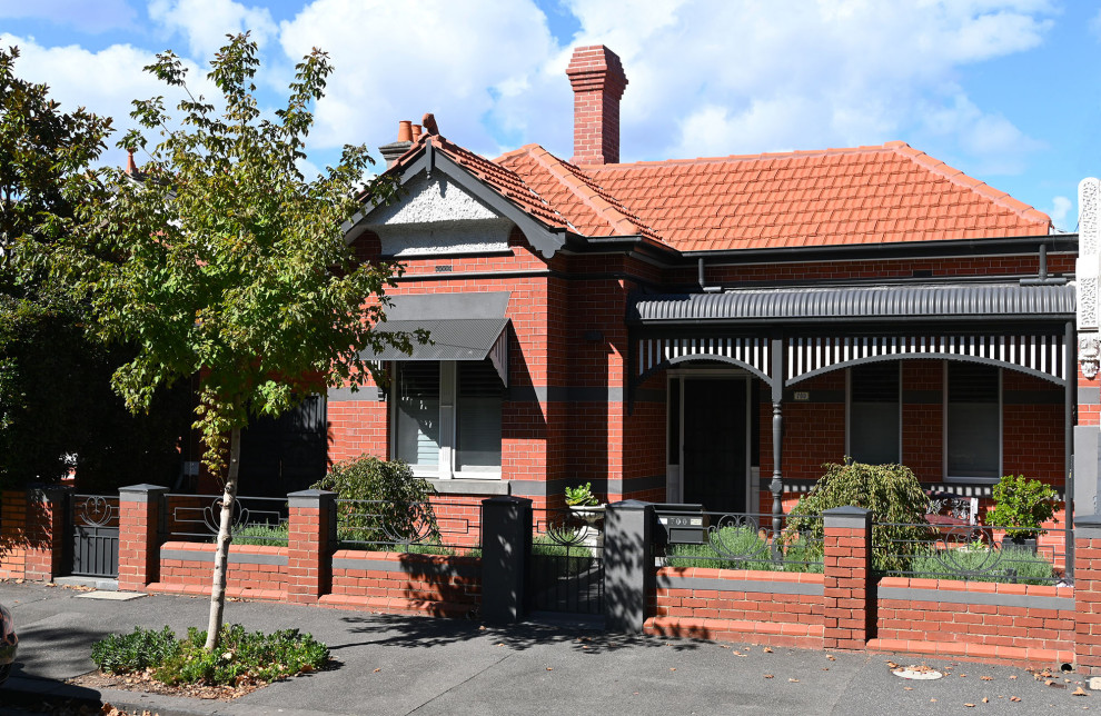 Aménagement d'une façade de maison rouge classique en brique de taille moyenne et de plain-pied avec un toit à quatre pans et un toit en tuile.