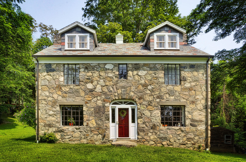 Photo of a gey rustic house exterior in New York with three floors, stone cladding and a pitched roof.