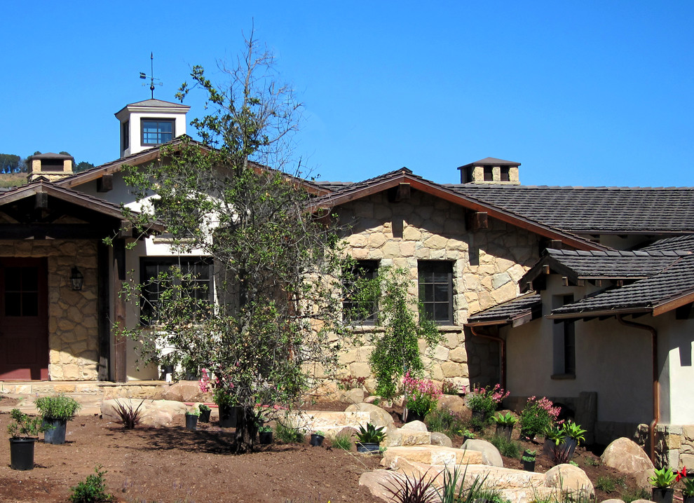 Idée de décoration pour une façade de maison beige champêtre en pierre de taille moyenne et de plain-pied avec un toit à deux pans et un toit en tuile.