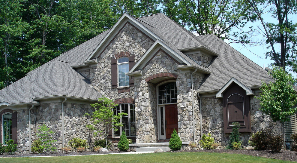 Aménagement d'une grande façade de maison grise classique en pierre à un étage avec un toit à quatre pans.