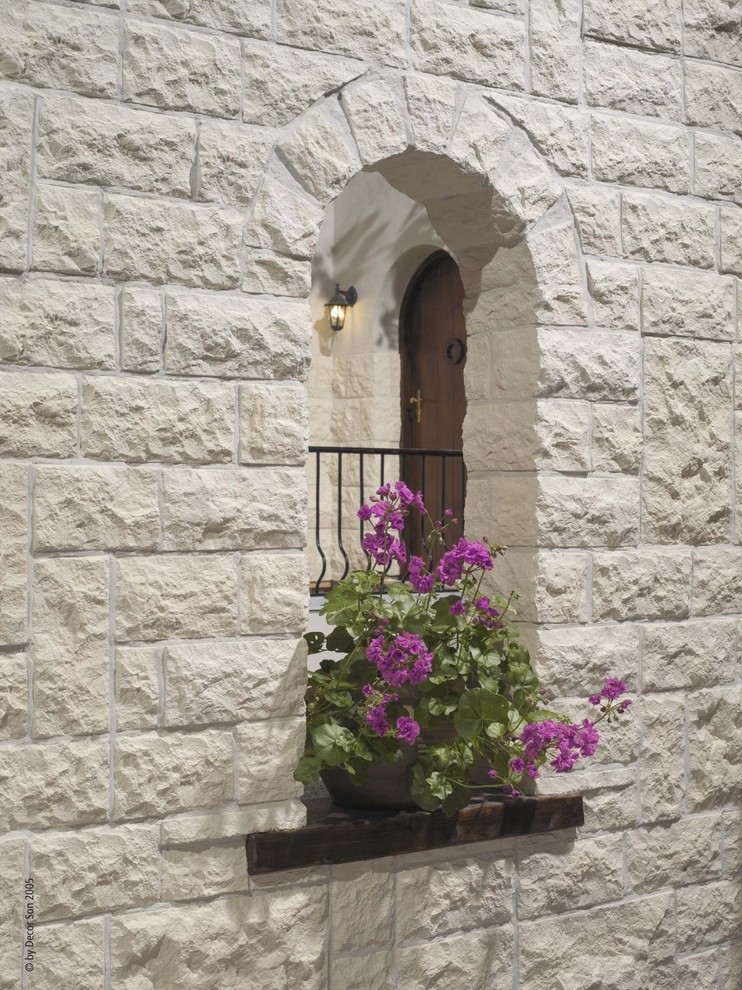 Esempio della facciata di una casa piccola bianca mediterranea a due piani con rivestimento in pietra