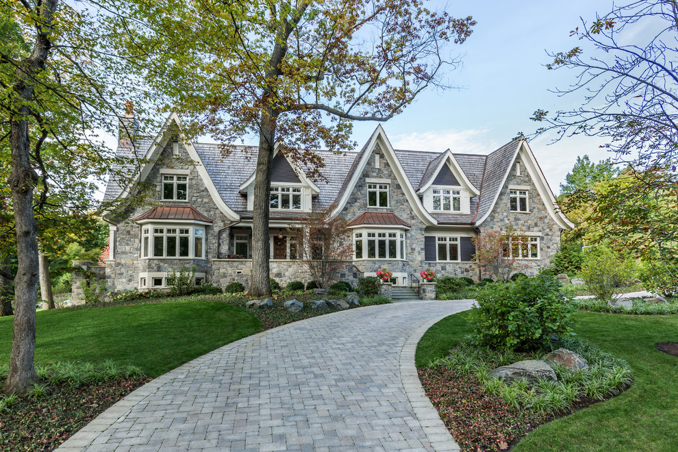 Пример оригинального дизайна: большой, трехэтажный, серый частный загородный дом с облицовкой из камня, двускатной крышей и крышей из смешанных материалов