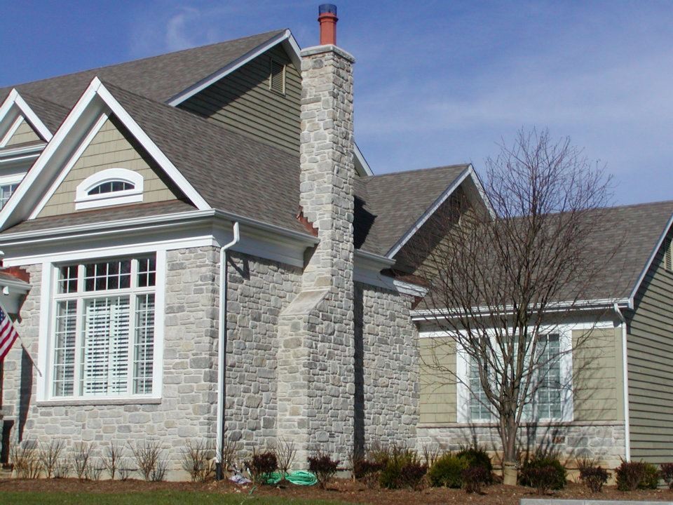 На фото: двухэтажный, серый частный загородный дом среднего размера в классическом стиле с облицовкой из камня и крышей из гибкой черепицы с
