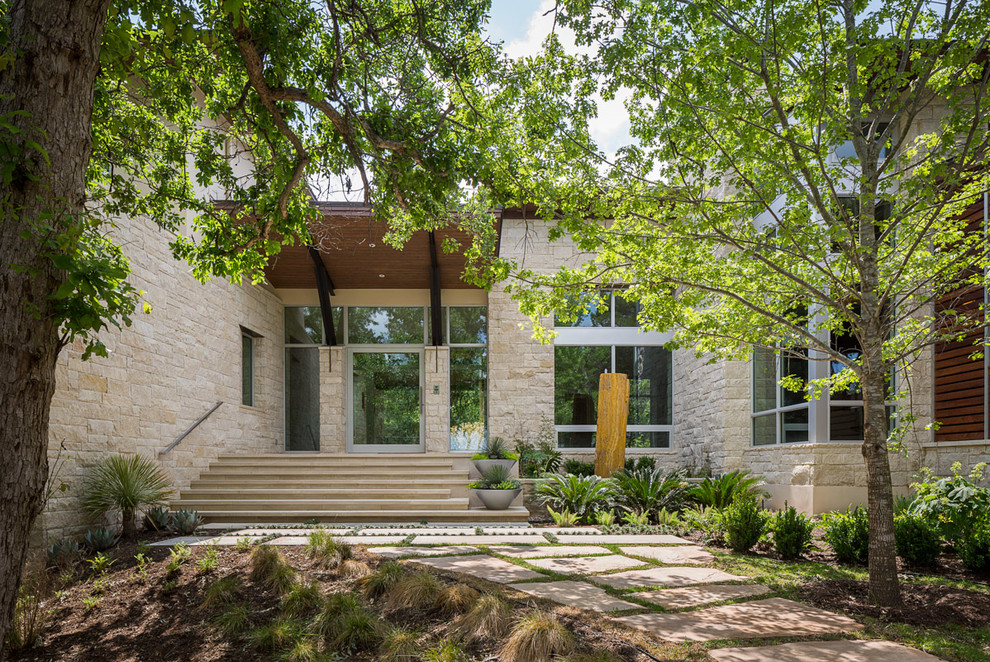 This is an example of a large and beige contemporary two floor house exterior in Austin with stone cladding and a lean-to roof.