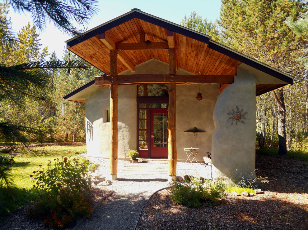 Пример оригинального дизайна: маленький, одноэтажный дом в стиле рустика с облицовкой из цементной штукатурки и двускатной крышей для на участке и в саду