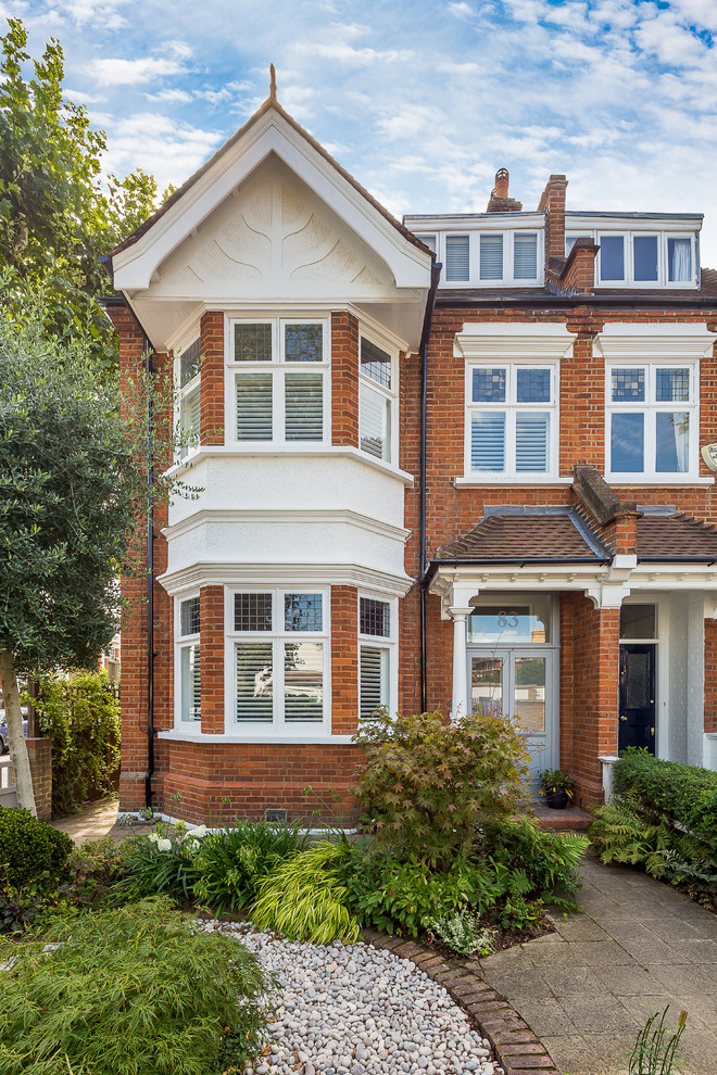 Large traditional red three-story brick duplex exterior idea in London with a hip roof