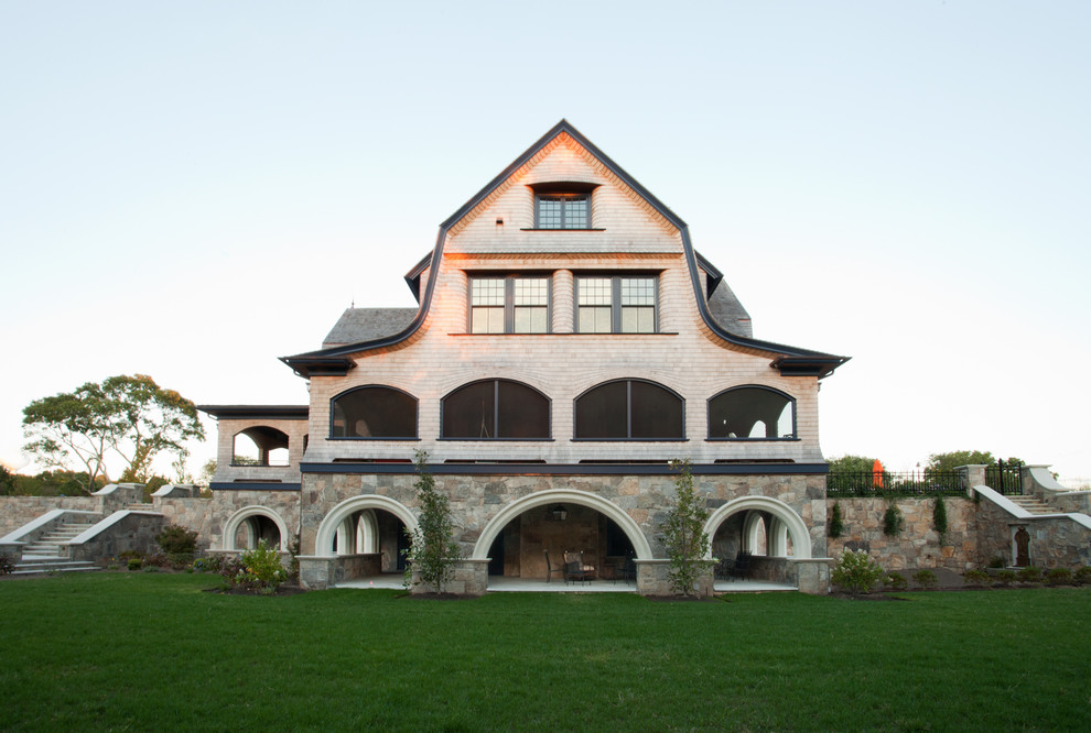 Esempio della villa ampia beige country a tre piani con rivestimento in legno, tetto a mansarda e copertura a scandole