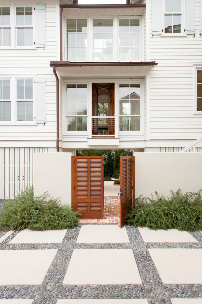Photo of a white beach style two floor house exterior in Charleston with wood cladding and a hip roof.