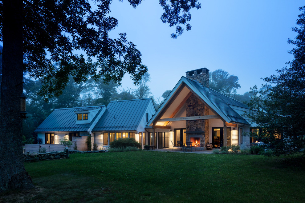 Immagine della villa grande bianca country a due piani con rivestimento in legno, tetto a capanna e copertura in metallo o lamiera