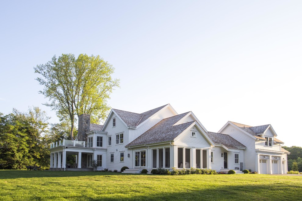 Immagine della villa ampia bianca classica a tre piani con rivestimento in legno, tetto a capanna e copertura a scandole