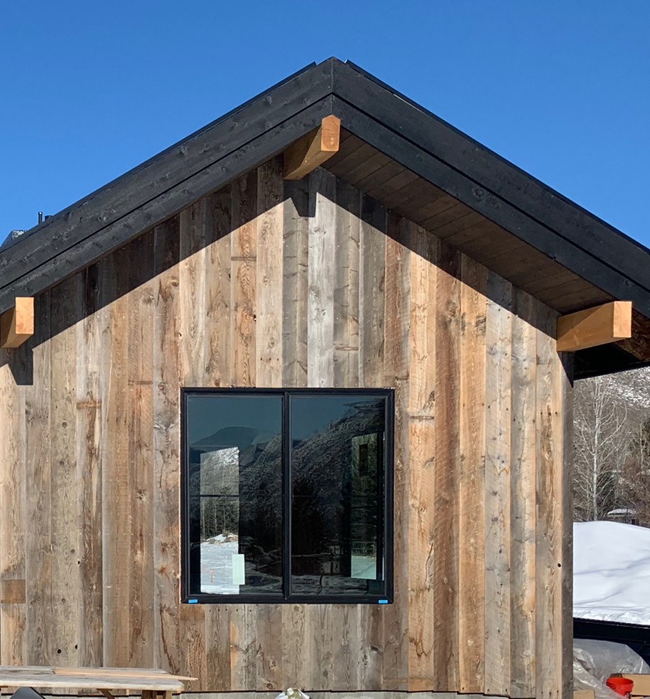 Réalisation d'une grande façade de maison grise champêtre en bois de plain-pied avec un toit à deux pans et un toit en métal.