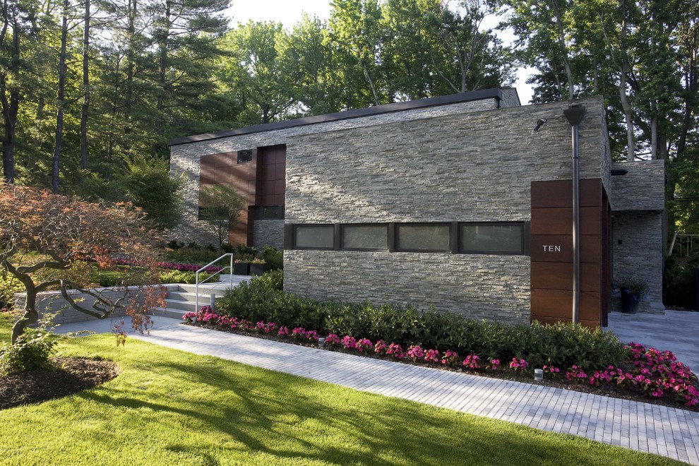 This is an example of a large and gey modern two floor house exterior in New York with stone cladding and a flat roof.