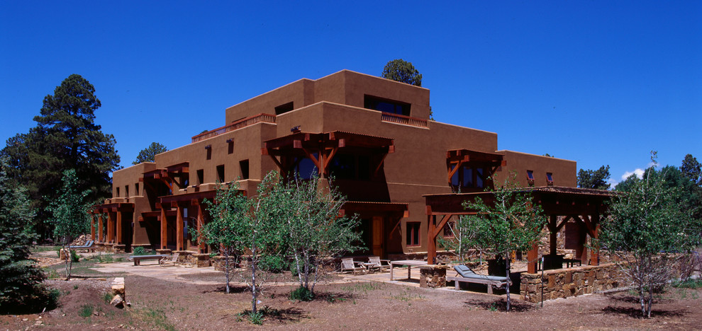 Cette image montre une grande façade de maison marron sud-ouest américain en stuc à deux étages et plus avec un toit plat.