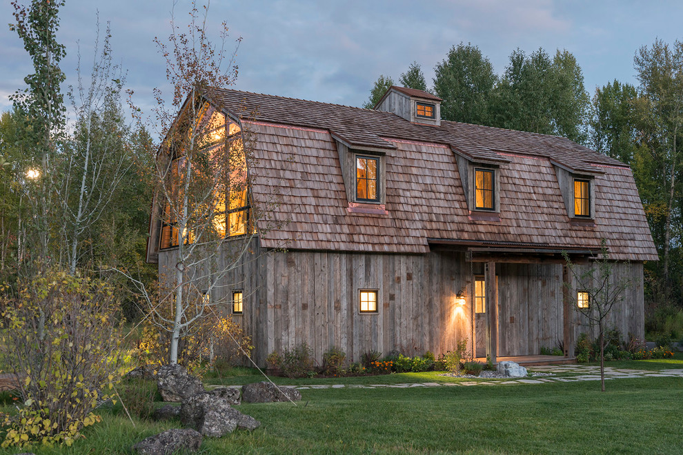 Esempio della facciata di una casa country a due piani con rivestimento in legno e tetto a mansarda