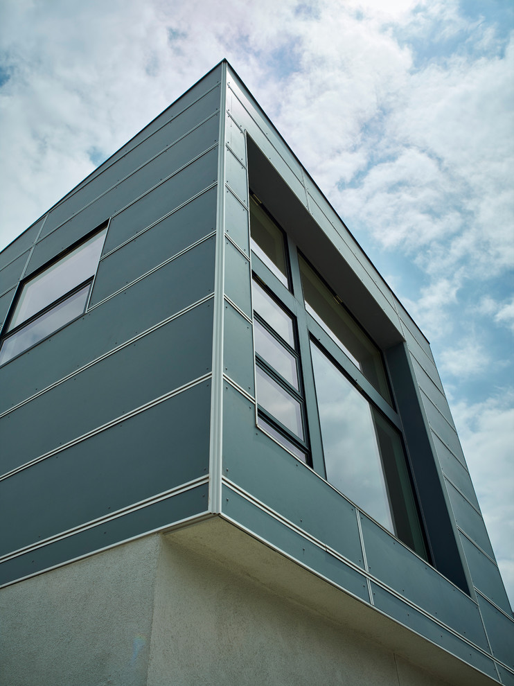 Cette image montre une grande façade de maison métallique et bleue design à un étage avec un toit plat.