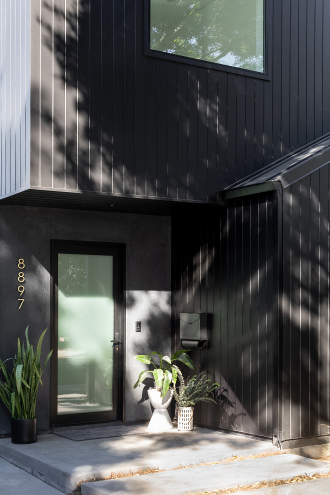 Foto på ett litet funkis svart hus, med två våningar, sadeltak och tak i metall