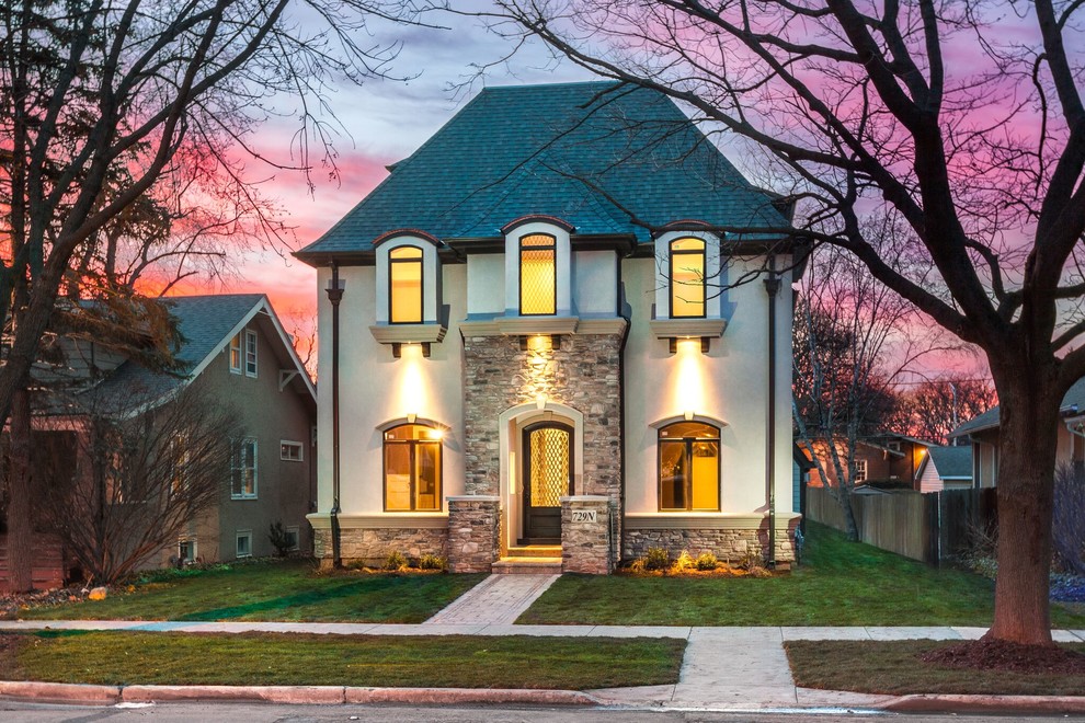 Large traditional beige two-story stucco house exterior idea in Chicago with a clipped gable roof and a mixed material roof
