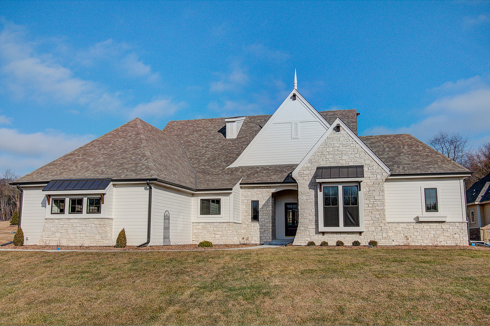 Large traditional beige one-story stone house exterior idea in Milwaukee with a hip roof and a mixed material roof