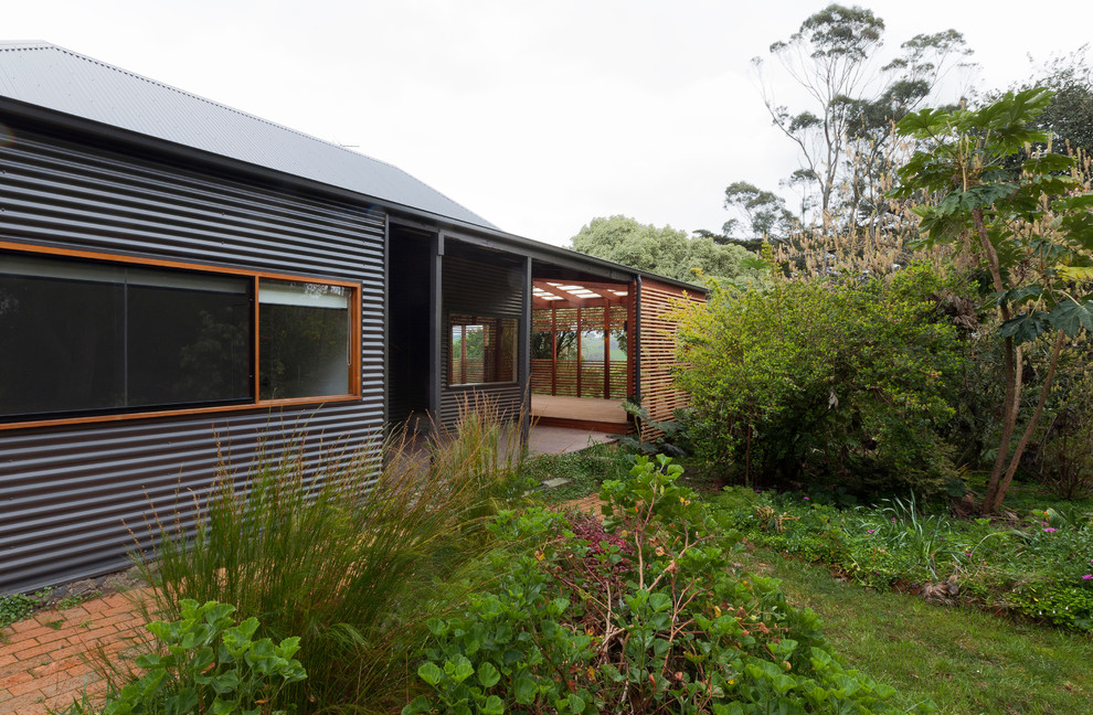 Cette photo montre une façade de maison grise et métallique tendance de taille moyenne et de plain-pied avec un toit à quatre pans.