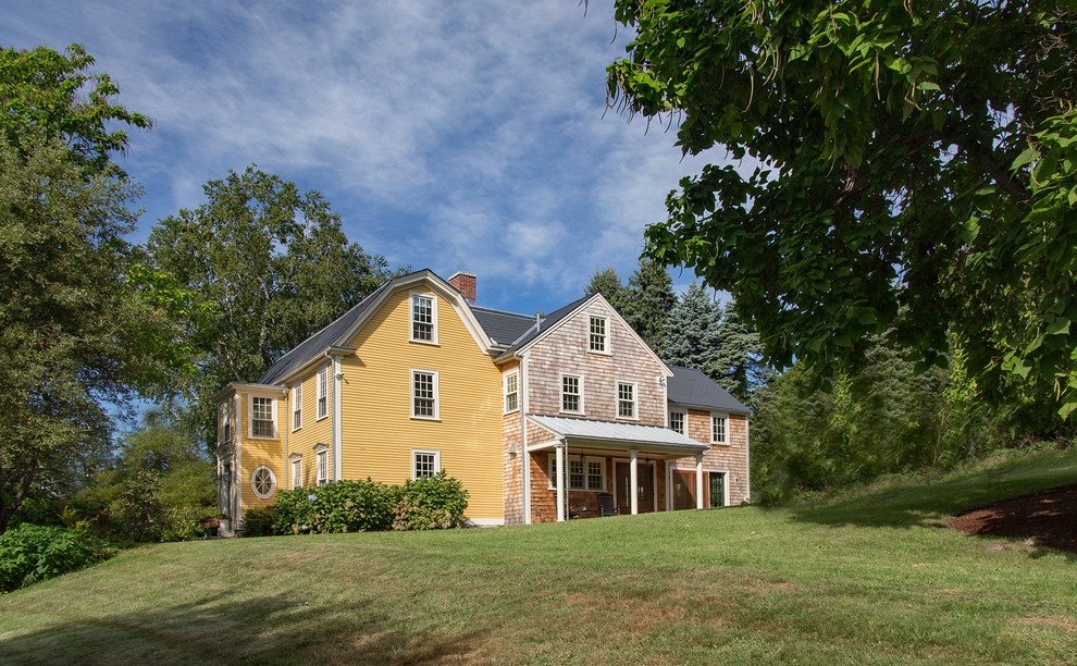 Modelo de fachada amarilla de estilo de casa de campo grande de tres plantas con revestimiento de madera