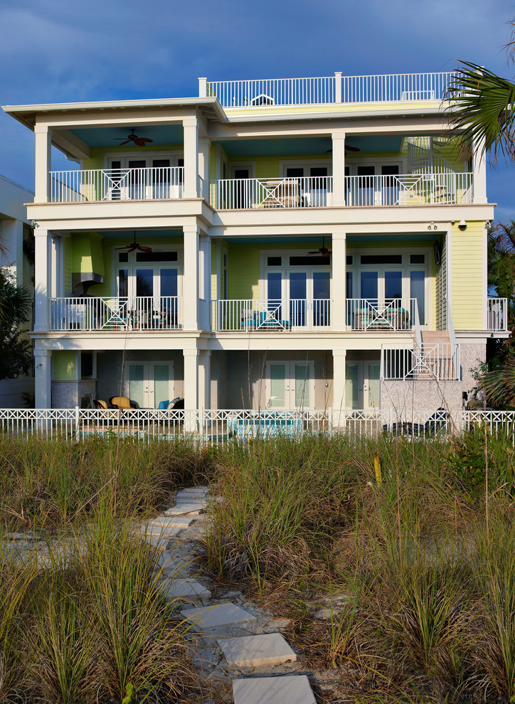 Foto della villa grande gialla tropicale a tre piani con rivestimento in legno, tetto piano e copertura in metallo o lamiera