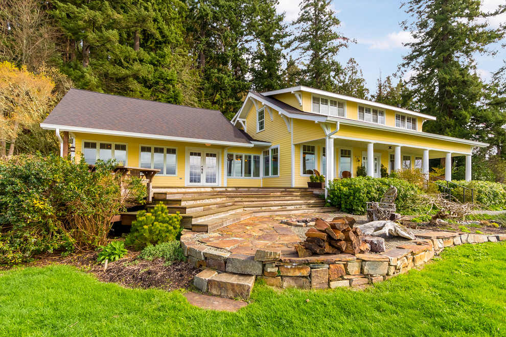 Esempio della facciata di una casa grande gialla country a due piani con rivestimento in legno e tetto a capanna