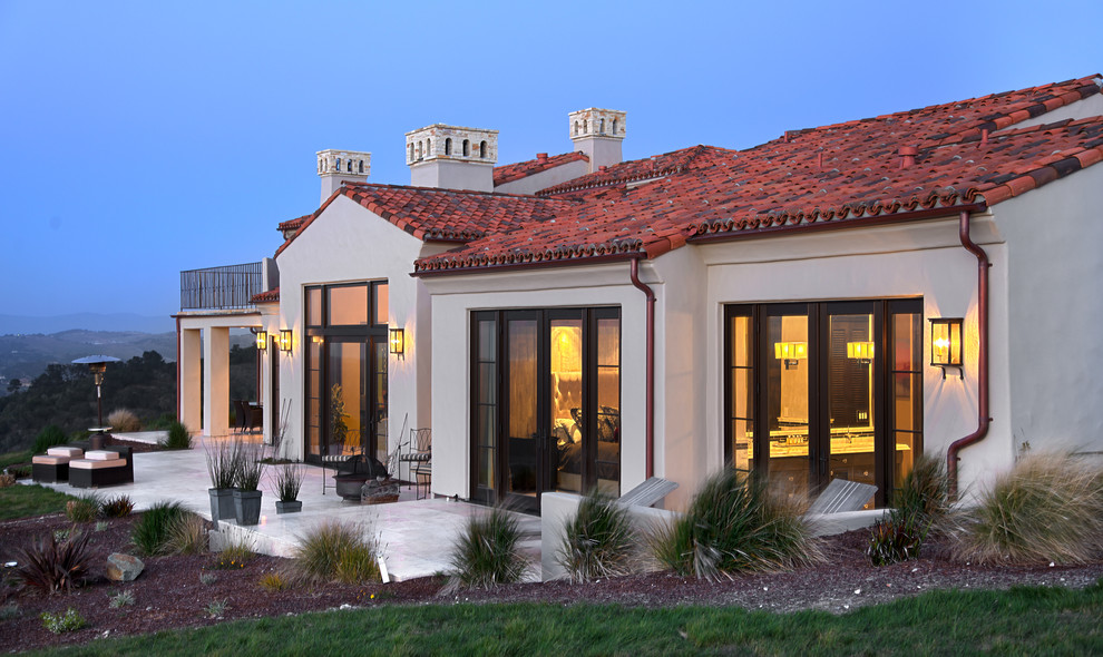 Modelo de fachada de casa beige mediterránea grande de una planta con revestimiento de adobe, tejado a dos aguas y tejado de teja de barro