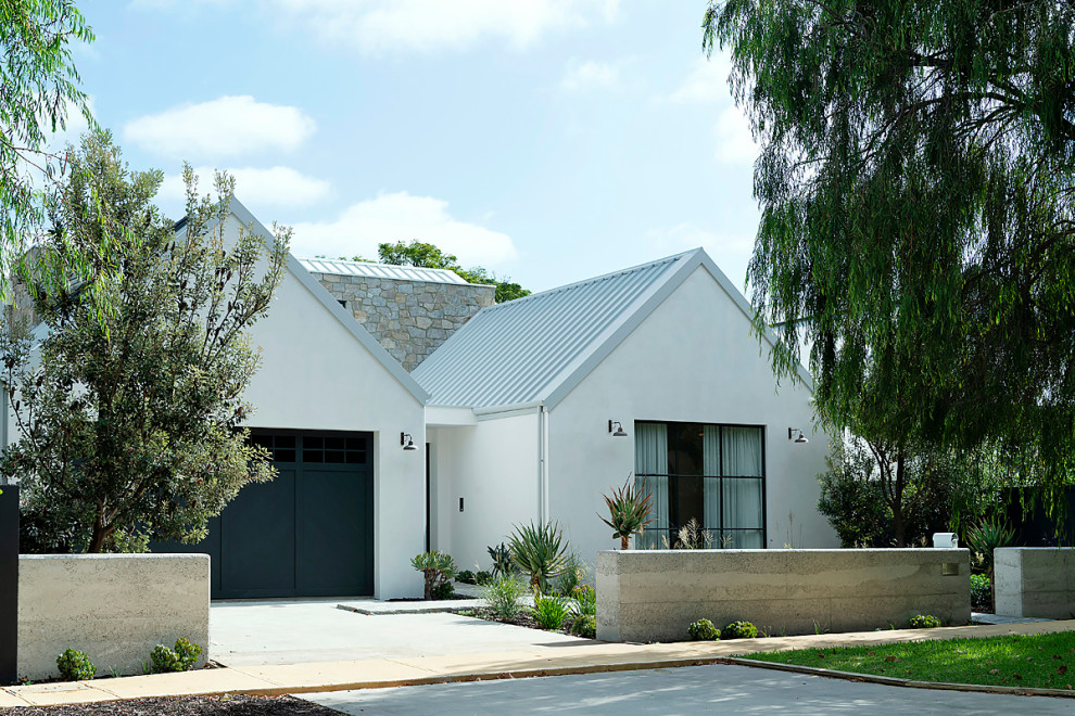 Cette photo montre une grande façade de maison blanche tendance en pierre à un étage avec un toit à deux pans et un toit en métal.