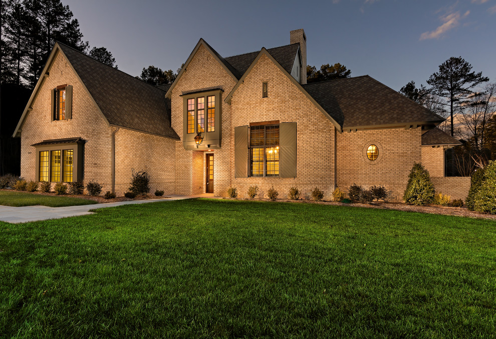 Large ornate beige two-story brick exterior home photo in Charlotte with a clipped gable roof