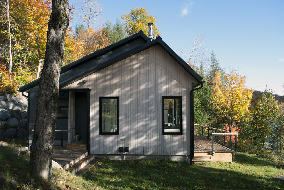 Photo of a small and gey scandinavian bungalow detached house in Montreal with wood cladding, a lean-to roof and a metal roof.