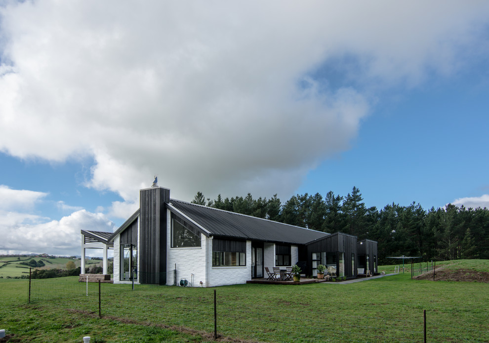 Immagine della villa bianca moderna a un piano di medie dimensioni con rivestimento in mattoni, tetto a capanna e copertura in metallo o lamiera